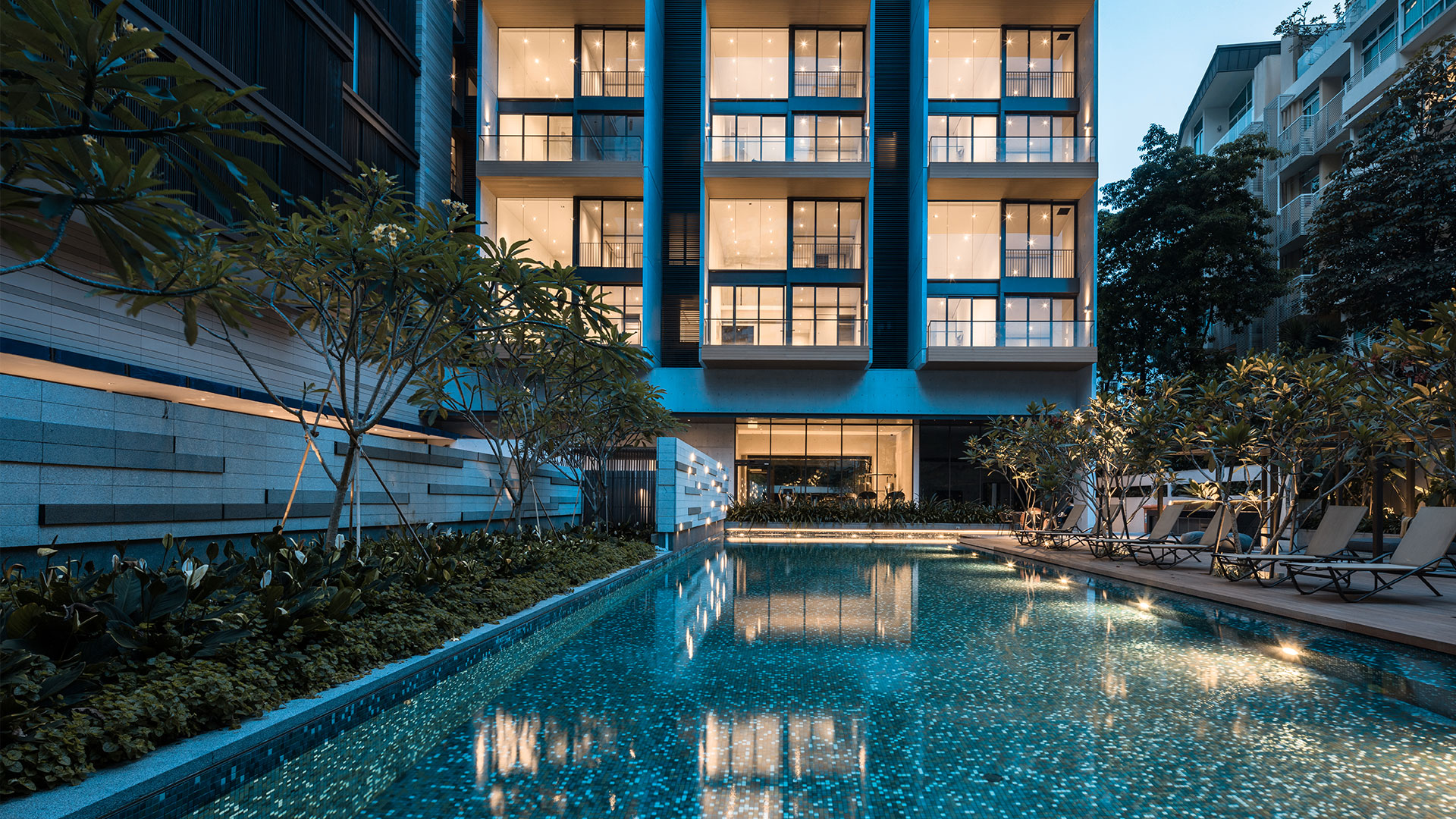 Evening exterior of Lloyd Sixtyfive, another TG Development project, with a lit facade and poolside garden