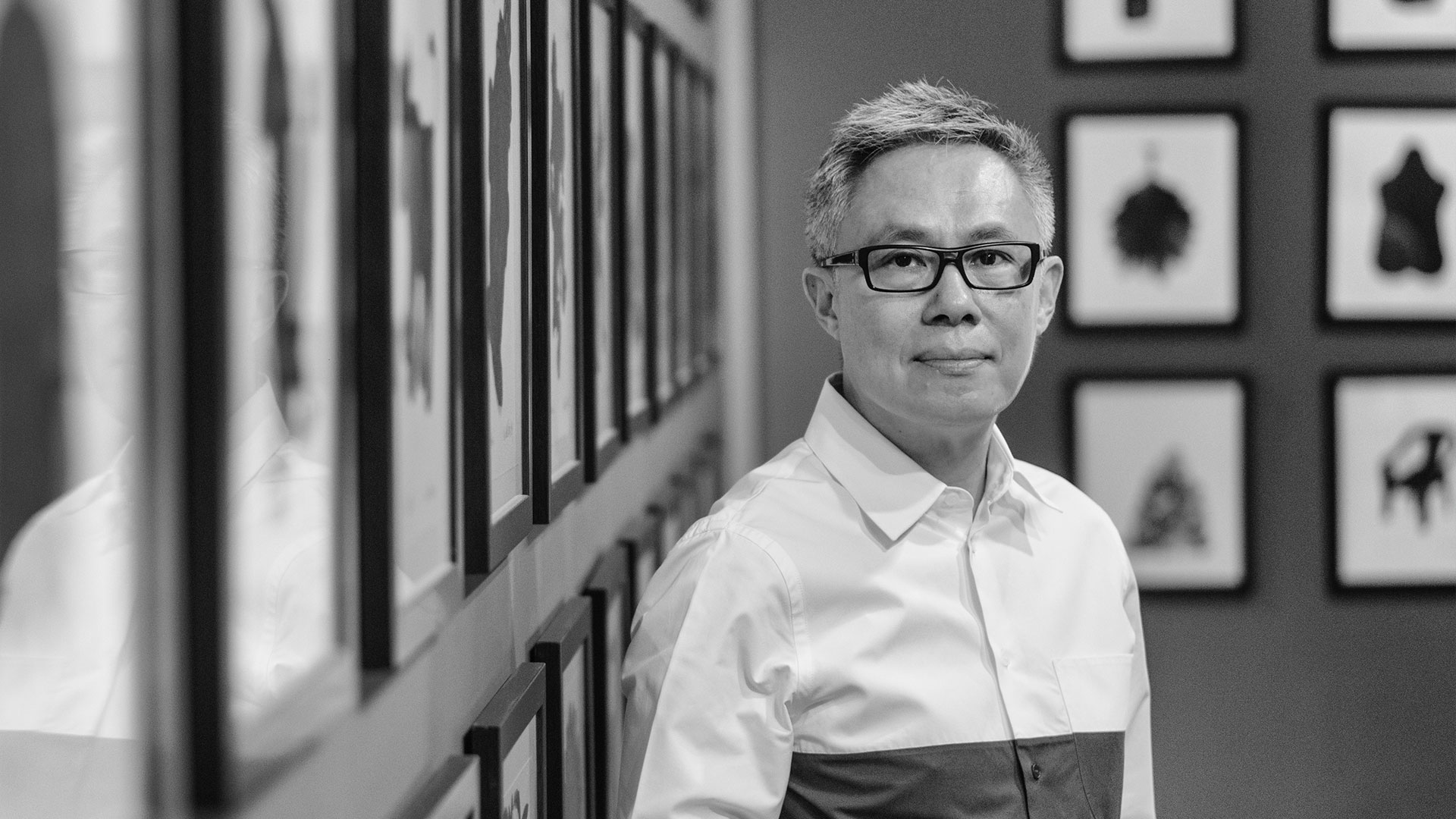 Portrait of The Oliv's architect standing beside a wall of framed artwork